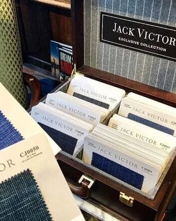 An open wooden Jack Victor fabric display case filled with swatch cards, alongside printed fabric swatch sheets showing blue and navy textile samples.