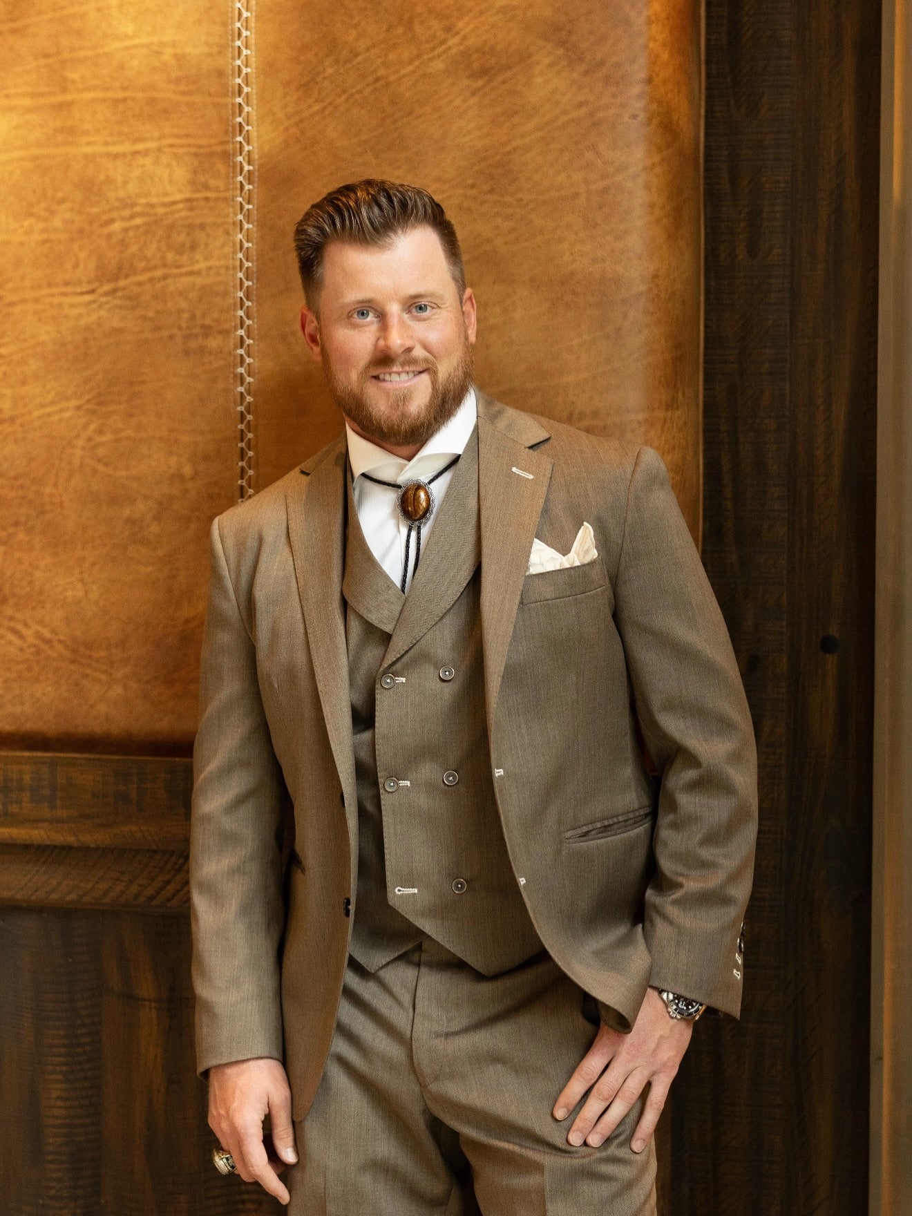 Man in a brown suit standing against a wooden background