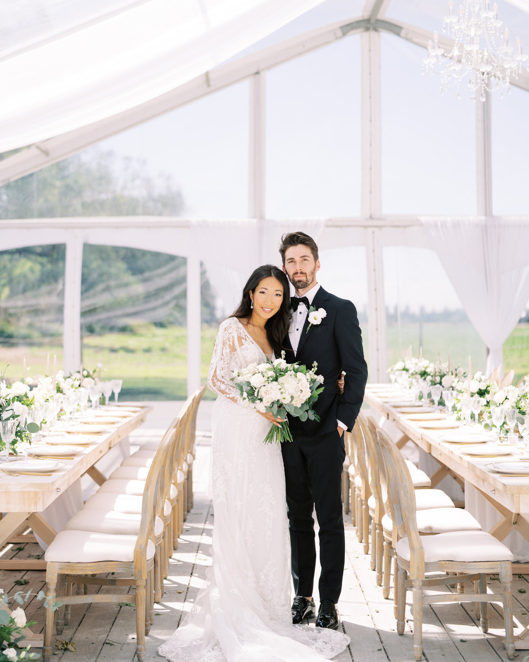 Wedding couple standing in a clear tent with a scenic background