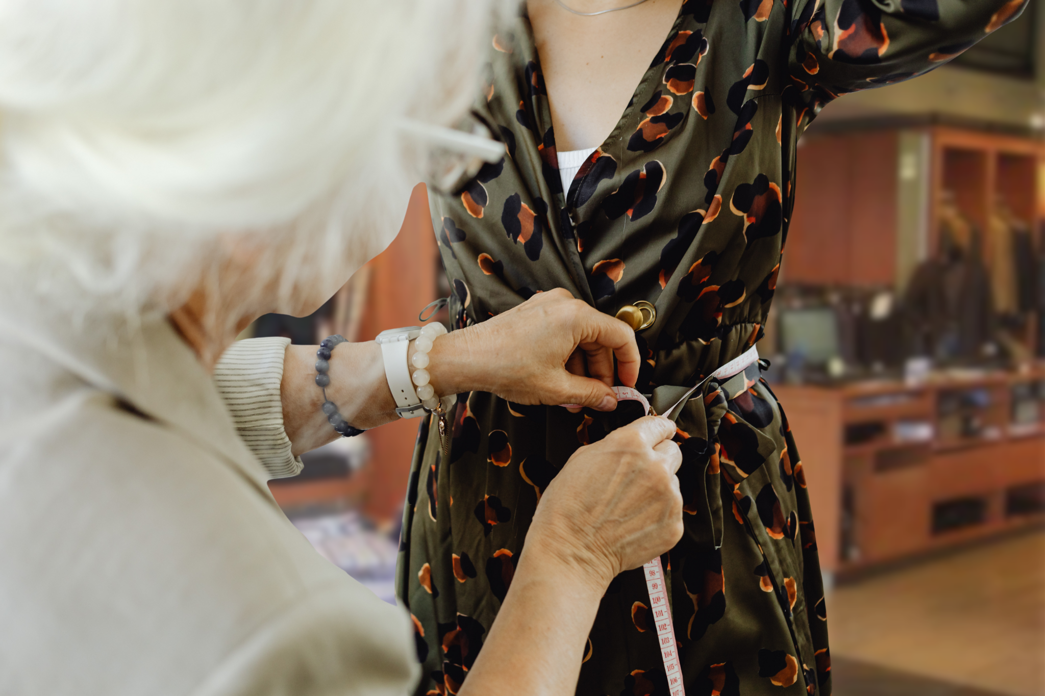 Person measuring a patterned dress with a tape measure in an indoor setting.