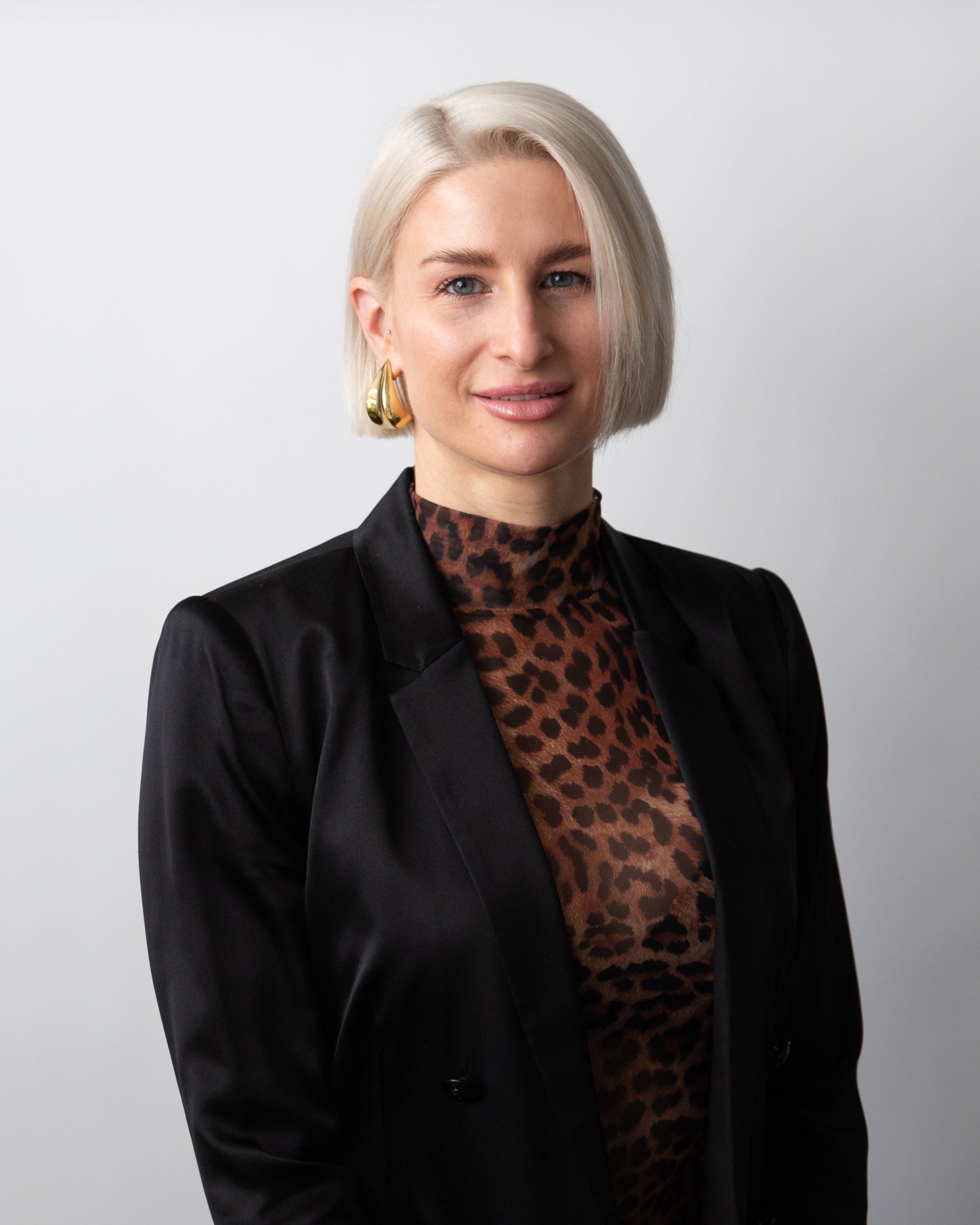 Nicole Oretan wearing a black blazer over a leopard print top against a plain background