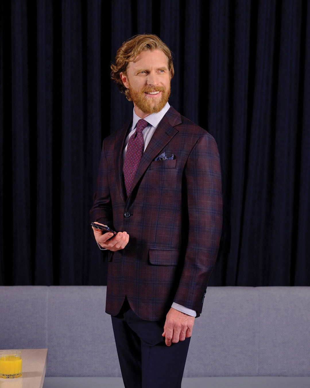 Man in a checkered suit standing against a dark curtain