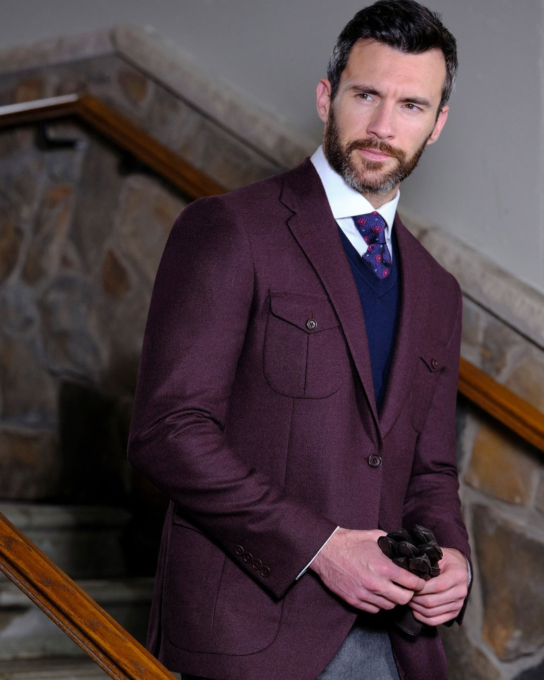Man wearing a burgundy suit standing in a room with stone walls.