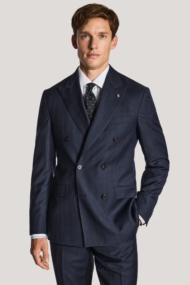 A man wearing a navy blue double-breasted suit with subtle pinstripes, a white dress shirt, and a patterned tie, standing against a light gray studio background.